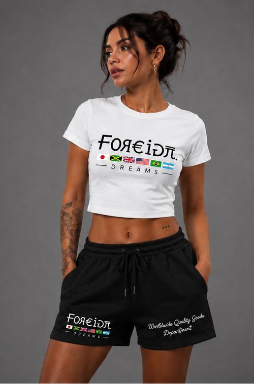 A woman modeling a white cropped t-shirt and black athletic shorts with 'FOREID' branding and colorful flag graphics, set against a solid gray studio background.